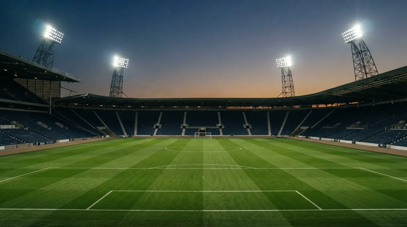 An empty football stadium with floodlight masts at dusk
